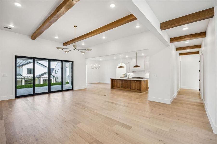 Unfurnished living room with a chandelier, light wood-style flooring, recessed lighting, and beamed ceiling Unfurnished living room with a chandelier, light wood-style flooring, recessed lighting, and beamed ceiling