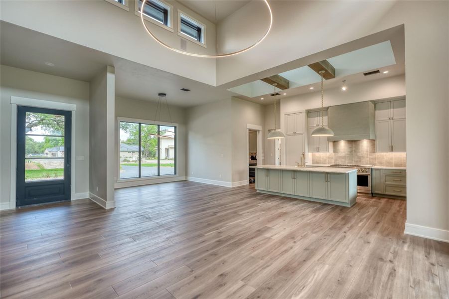 Unfurnished living room with a high ceiling, a sink, baseboards, and light wood finished floors