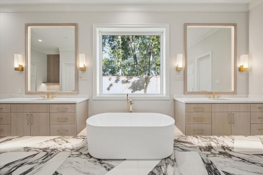 Retreat-like and thoughtfully designed, the primary bath showcases sleek double floating vanities with custom framed mirrors, sculptural sconces, and refined brass accents. Quartz countertops add timeless luxury, while a freestanding soaking tub sits beside a large picture window enhancing its overall sense of serenity.