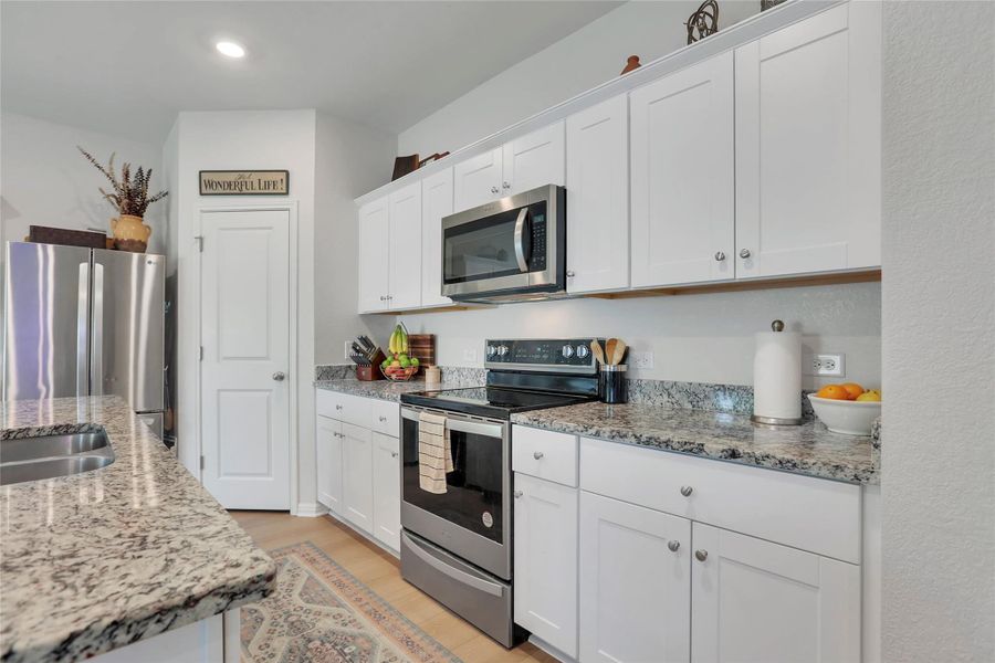 Kitchen with stainless steel appliances, white cabinets, light stone counters, and light wood-style floors