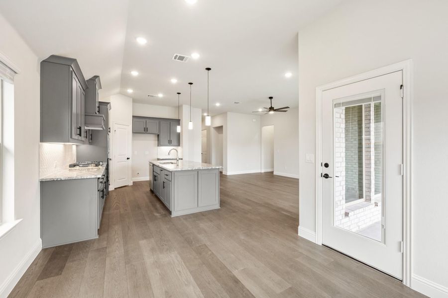 Open kitchen with gray cabinets, center island, light wood floors, and pendant lights opening to living area Open kitchen with gray cabinets, center island, light wood floors, and pendant lights opening to living area