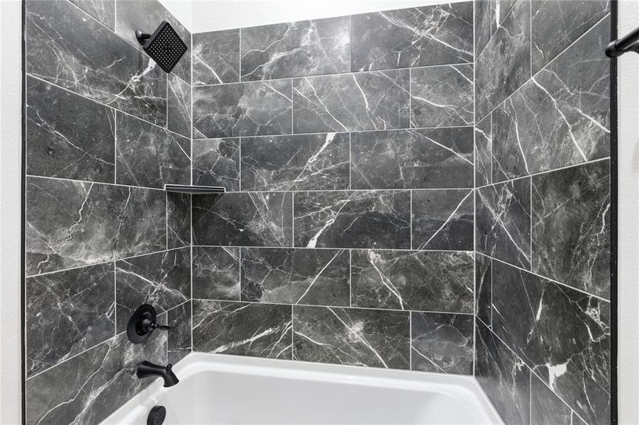 Bathtub and shower combination featuring dark-toned, large format tile with white veining