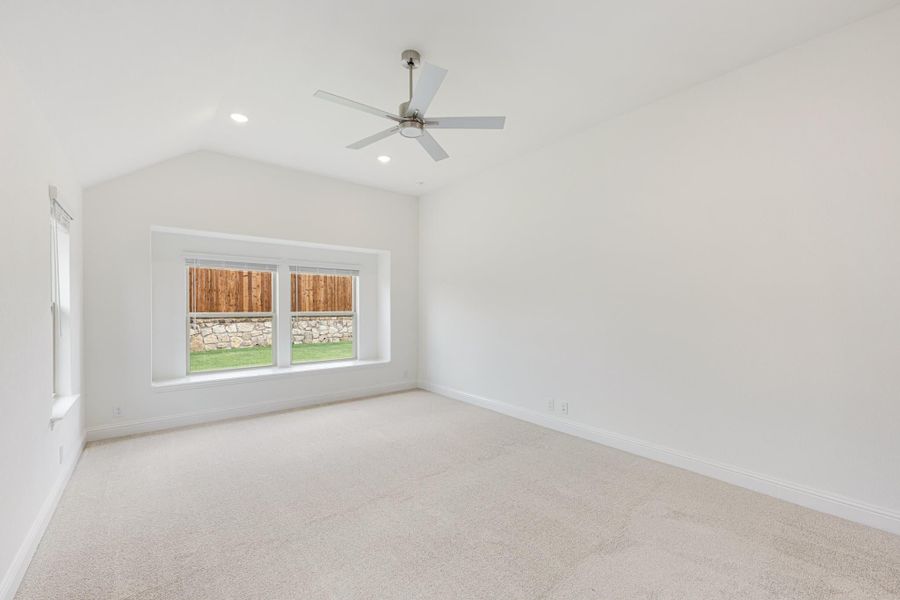 Empty bedroom with vaulted ceiling, ceiling fan, carpet flooring, and large window overlooking backyard Empty bedroom with vaulted ceiling, ceiling fan, carpet flooring, and large window overlooking backyard
