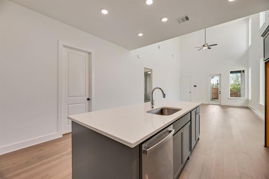Kitchen featuring dishwasher, light wood finished floors, a towering ceiling, a kitchen island with sink, and gray cabinets Kitchen featuring dishwasher, light wood finished floors, a towering ceiling, a kitchen island with sink, and gray cabinets