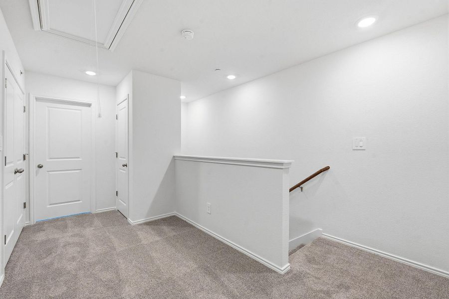 Carpeted landing with white walls and trim, recessed lighting, and a wooden handrail Carpeted landing with white walls and trim, recessed lighting, and a wooden handrail