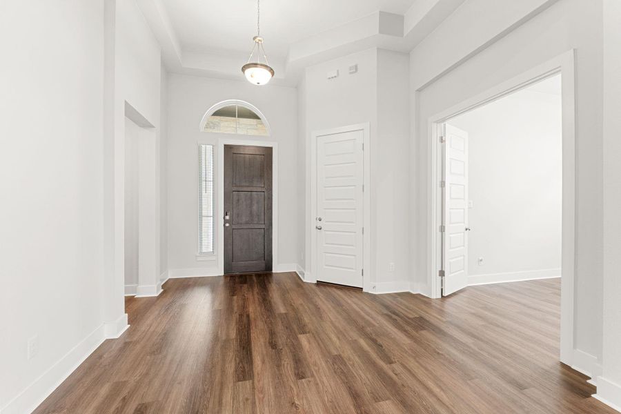 Entrance foyer featuring wood finished floors, baseboards, a tray ceiling, and a towering ceiling Entrance foyer featuring wood finished floors, baseboards, a tray ceiling, and a towering ceiling