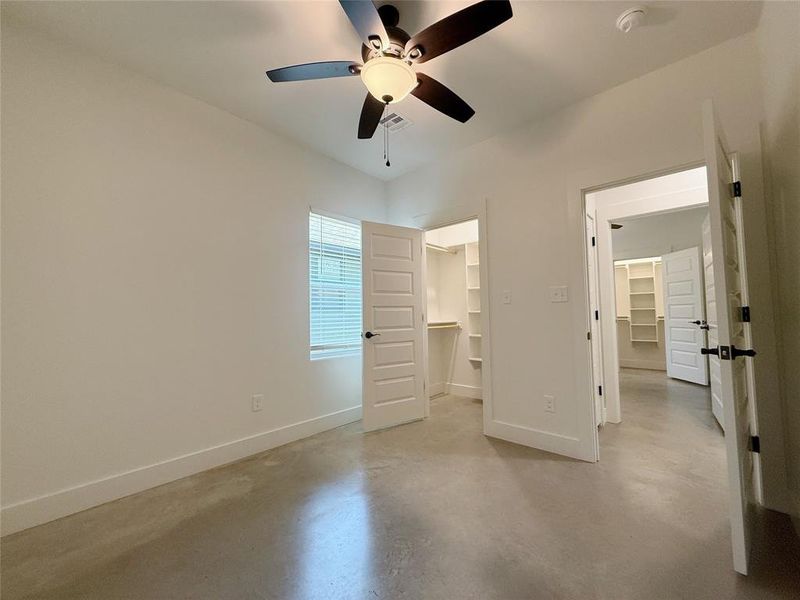 Unfurnished bedroom featuring a spacious closet, concrete floors, and ceiling fan