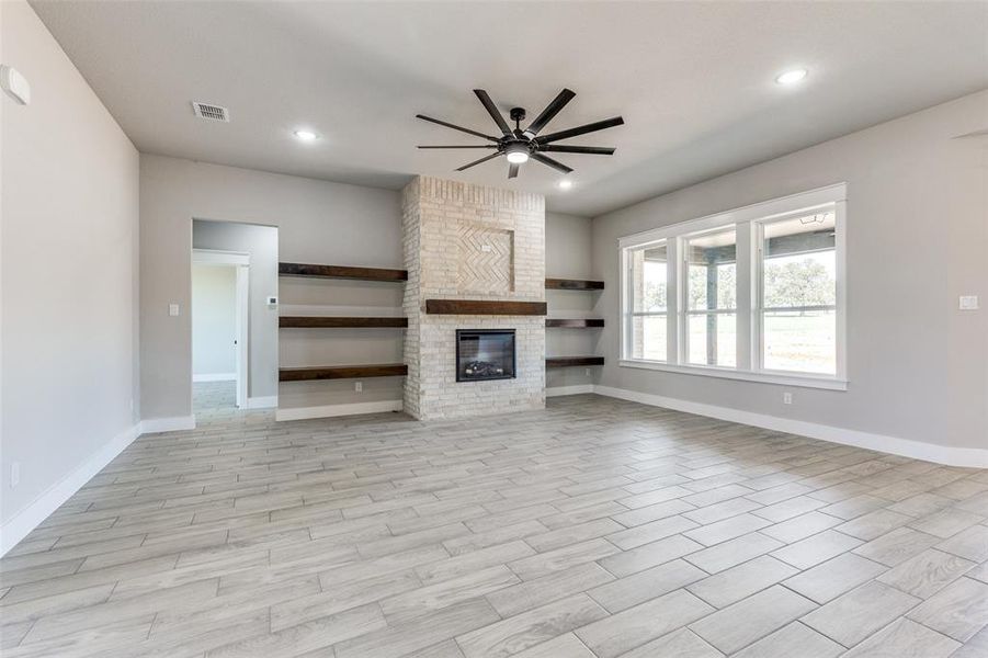 Unfurnished living room featuring a brick fireplace, ceiling fan, and light wood-type flooring