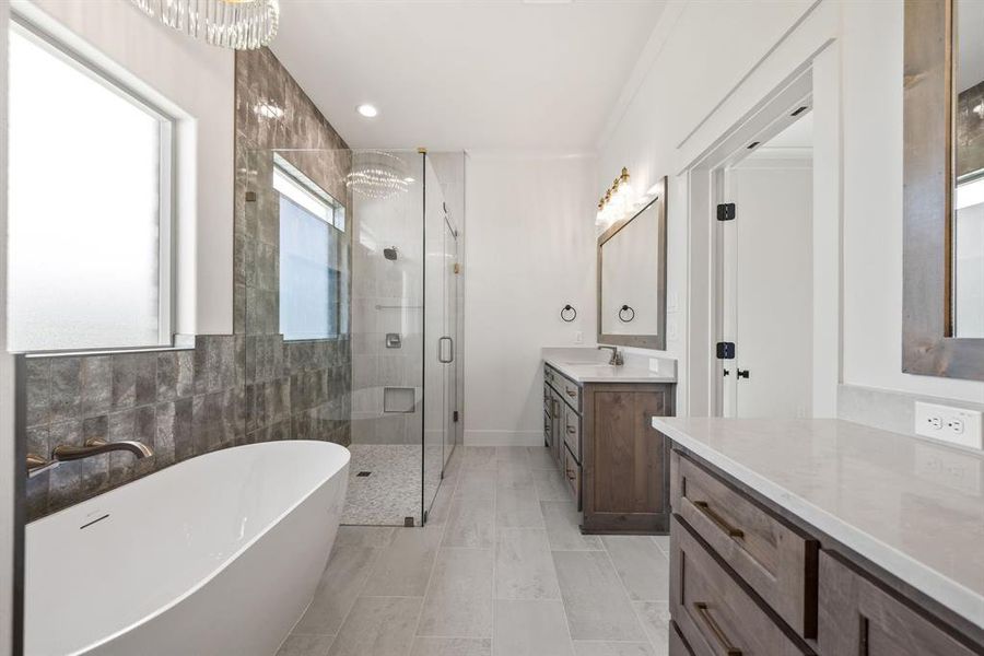 Contemporary bathroom featuring a freestanding soaking tub, a frameless glass shower with stone-look tile, and two separate vanities with stone countertops and wood-finish cabinetry