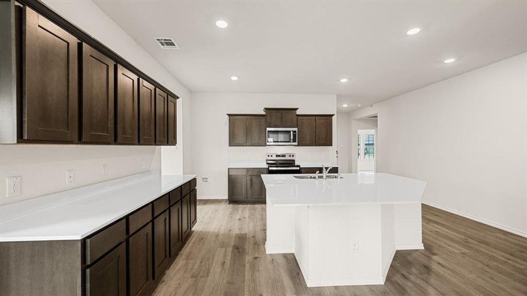 Kitchen featuring dark wood-finish cabinetry, white countertops, stainless steel appliances, a center island with sink, and recessed lighting Kitchen featuring dark wood-finish cabinetry, white countertops, stainless steel appliances, a center island with sink, and recessed lighting