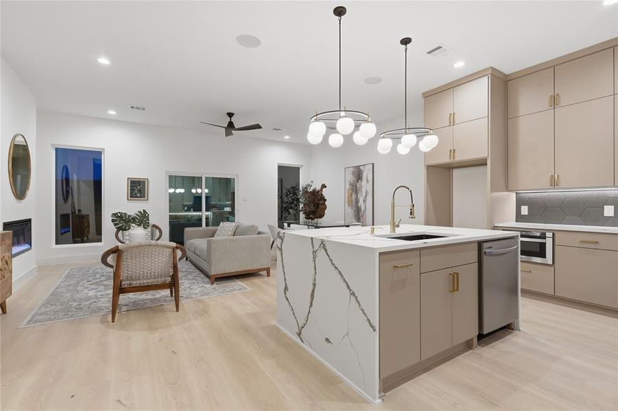 Open-concept living space featuring light wood-finish flooring, a modern kitchen island with integrated sink, and recessed lighting