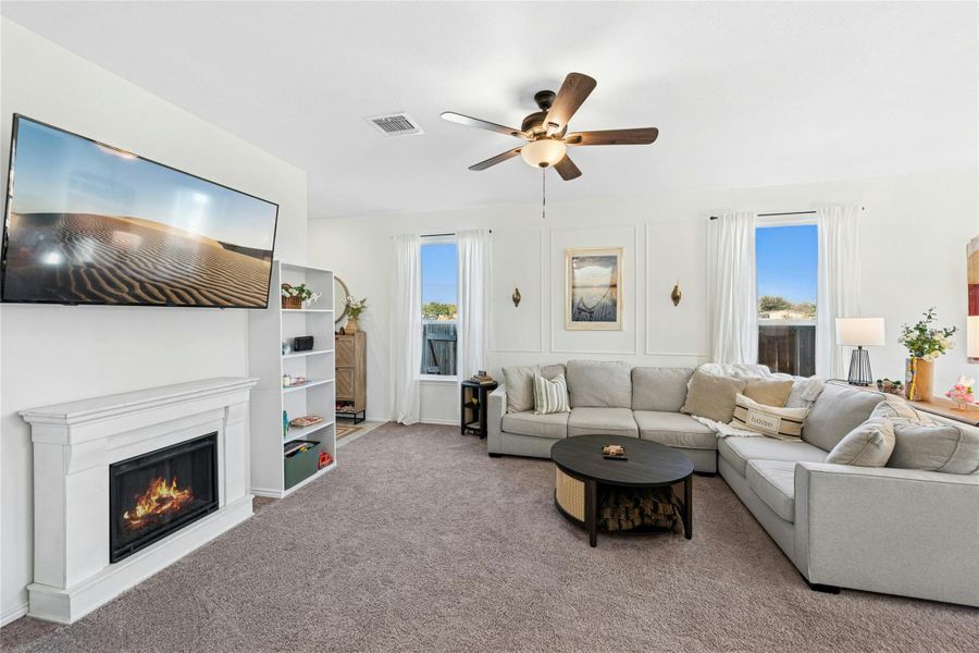 A cozy living area filled with natural light, featuring a gas fireplace flanked by decorative built-ins. This inviting space also includes carpet flooring and a ceiling fan, creating a warm and comfortable atmosphere perfect for everyday living and relaxation.