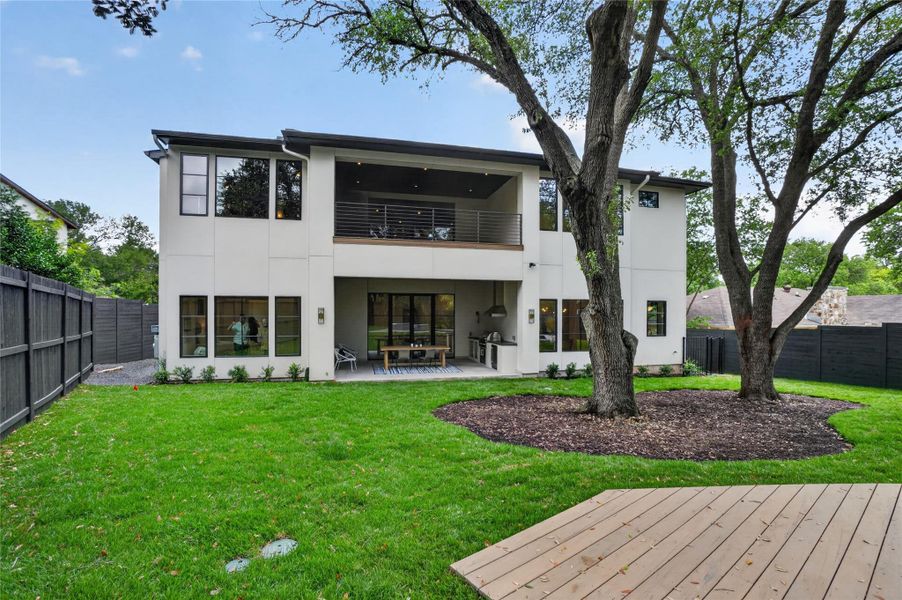 A spacious backyard unfolds, featuring a covered patio, balcony, and lush green lawn.