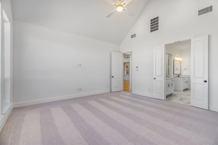 Unfurnished bedroom featuring vaulted ceiling, light colored carpet, a ceiling fan, and ensuite bath