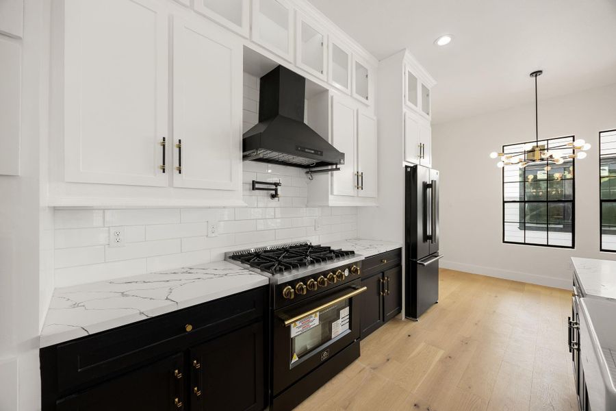 A stunning kitchen featuring a touchless vent hood, gas range, beautiful quartz countertops, custom cabinetry hardware. Thoughtful finishes throughout add a sophisticated, elevated touch to this beautifully appointed space.