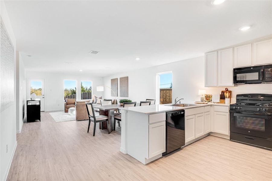 Kitchen with black appliances, kitchen peninsula, sink, light hardwood / wood-style floors, and white cabinetry