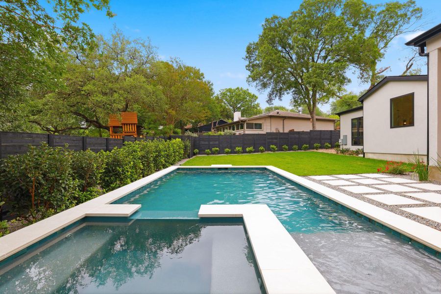 Outdoor living space featuring a rectangular pool with integrated spa, bordered by a large grass lawn and mature trees