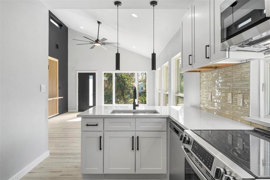 Kitchen with appliances with stainless steel finishes, a peninsula, recessed lighting, decorative light fixtures, and light wood finished floors