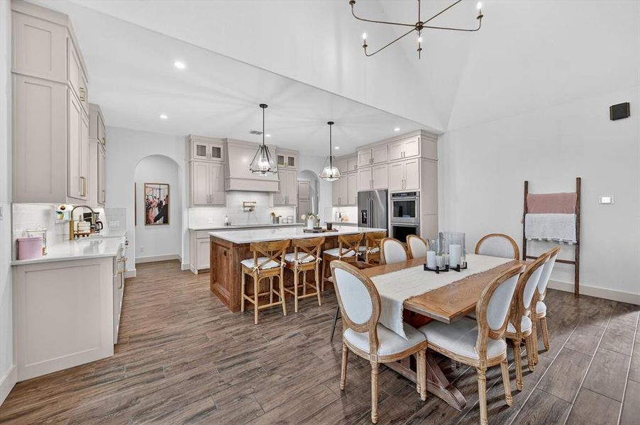 Open-concept kitchen and dining area featuring light-toned cabinetry, built-in stainless steel appliances, a wood-finish island with seating, and wood-finish flooring