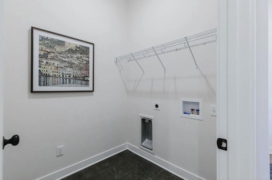 Dedicated laundry area featuring white walls, wire shelving, and a dark tile floor