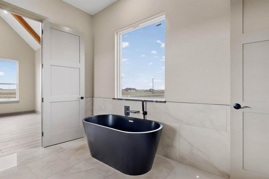 Bathroom featuring a freestanding tub, healthy amount of natural light, and tile walls Bathroom featuring a freestanding tub, healthy amount of natural light, and tile walls
