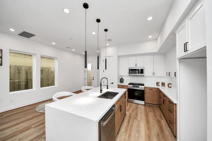 Discover the heart of this home in a sleek, modern kitchen boasting elegant white cabinetry, warm wood accents, and a spacious island perfect for culinary creations and gatherings.