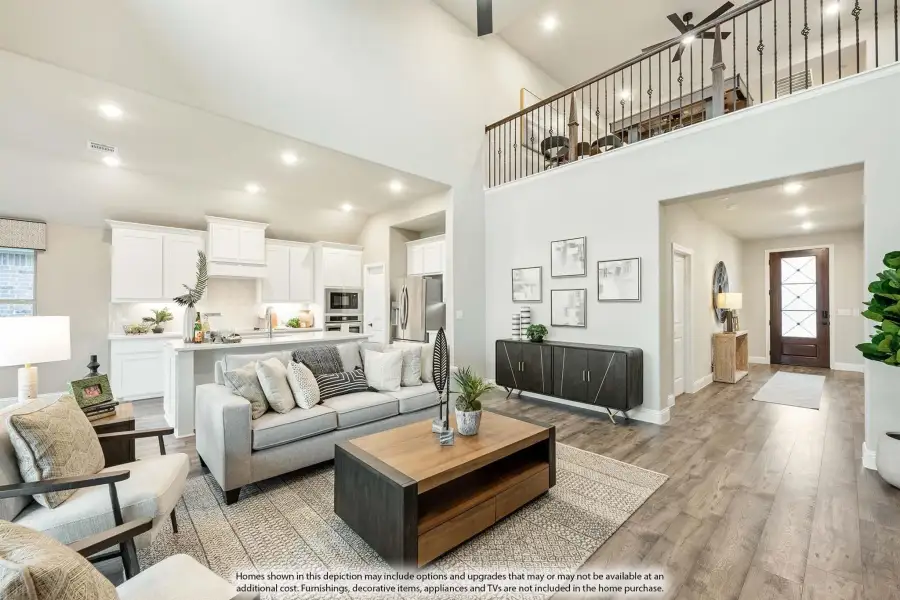 Open living room with vaulted ceiling, wood floors, and open-concept kitchen with white cabinets and upstairs loft railing visible.