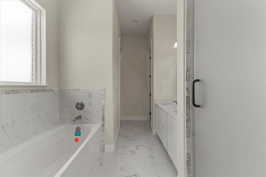 Bathroom featuring marble finish floors, a garden tub, and vanity