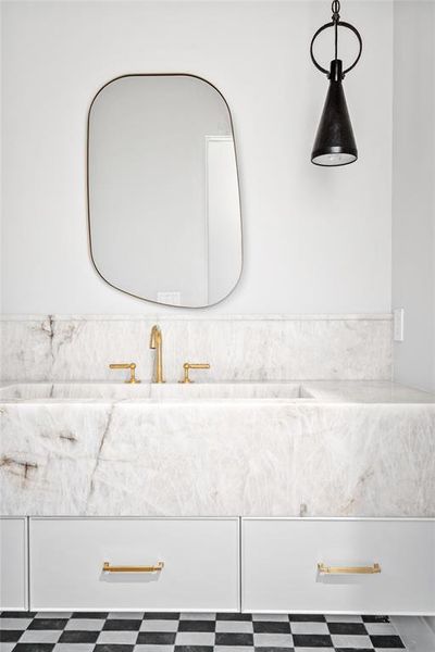 An upstairs powder room showcases a Cristallo Quartzite vanity with an integrated sink and sleek under-mount drawers. Overhead, Suzanne Kasler natural rusted iron pendants add a touch of industrial charm, while classic cottage checkered tile floors bring a timeless, vintage-inspired appeal to the space.