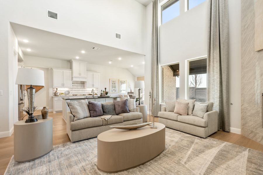 Open-concept living room with two-story ceilings, neutral sofas, and kitchen visible in background