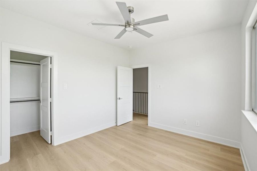 Unfurnished bedroom featuring light wood finished floors, a walk in closet, baseboards, a closet, and a ceiling fan