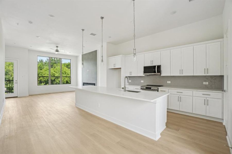 Kitchen with stainless steel appliances, a sink, backsplash, light wood-style floors, and white cabinetry