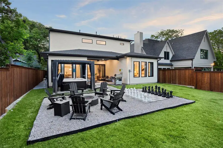 Modern residence featuring a manicured lawn, a gravel patio with a built-in fire pit, and a covered hot tub area