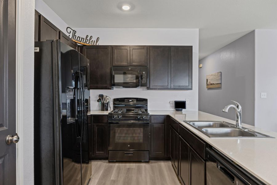 Kitchen with black appliances, a peninsula, light quartz countertops, LVP flooring, and dark brown cabinetry Kitchen with black appliances, a peninsula, light quartz countertops, LVP flooring, and dark brown cabinetry