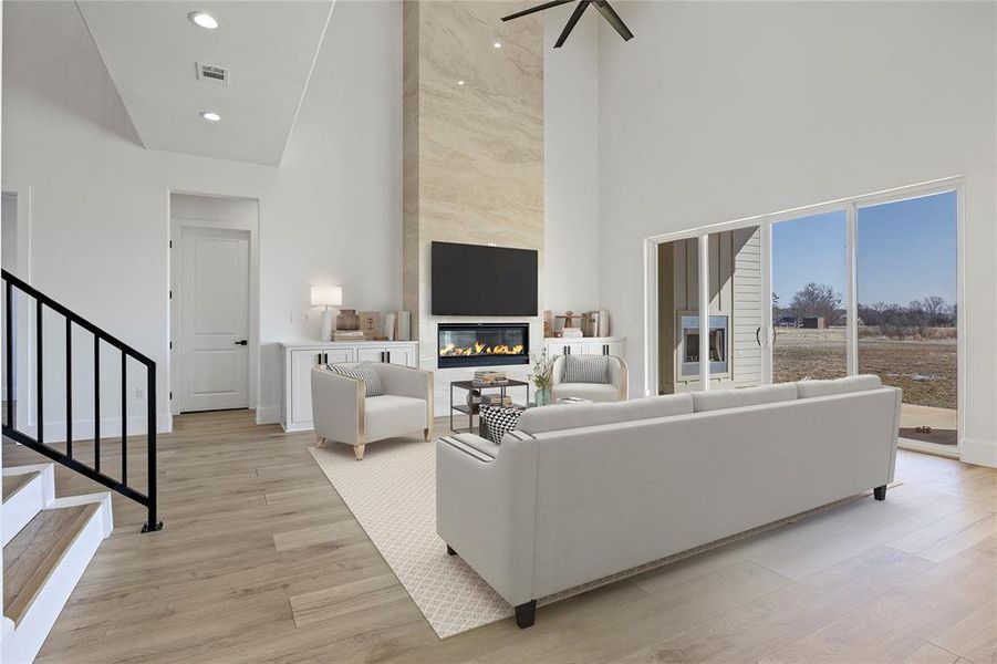 Living room featuring visible vents, a towering ceiling, stairs, light wood-style flooring, and a premium fireplace Living room featuring visible vents, a towering ceiling, stairs, light wood-style flooring, and a premium fireplace