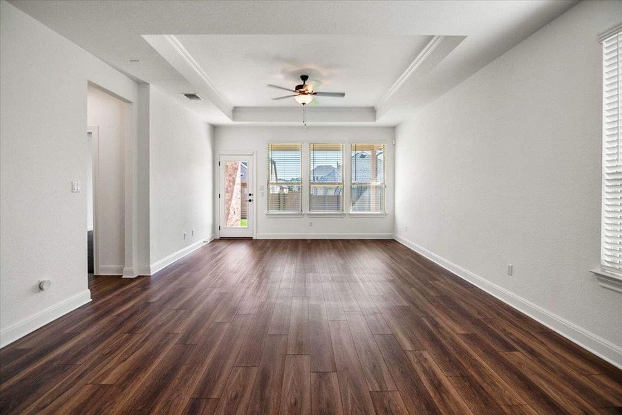 Rich hardwood-style flooring extends through this airy living space with a classic tray ceiling and well-lit windows.