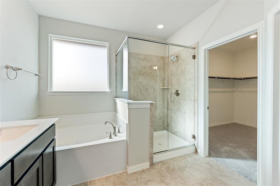 Full bathroom featuring a bath, a walk in closet, vanity, a stall shower, and light carpet