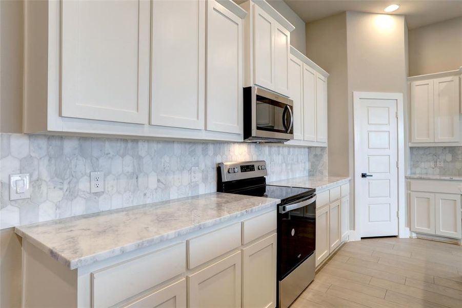 Kitchen featuring tasteful backsplash, appliances with stainless steel finishes, light stone countertops, and white cabinets