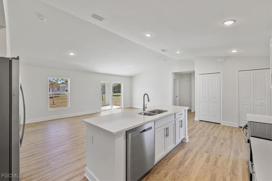 Kitchen with appliances with stainless steel finishes, lofted ceiling, white cabinets, open floor plan, and light wood finished floors