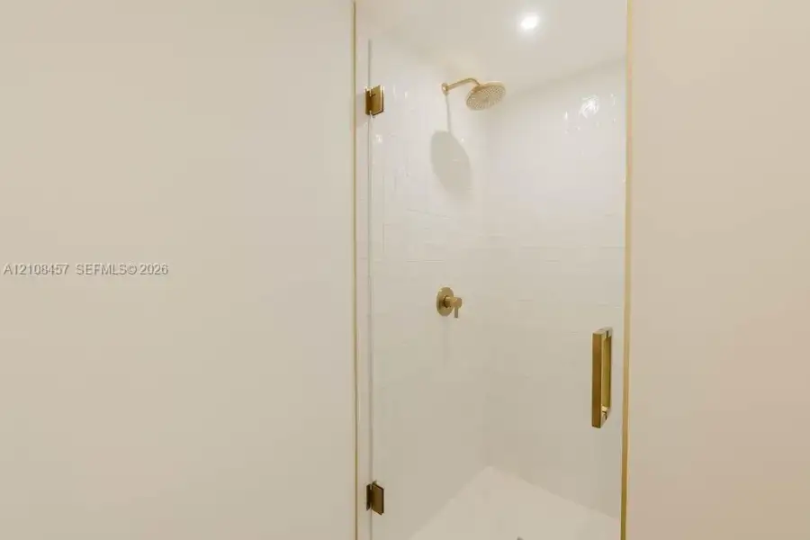 Walk-in shower featuring a frameless glass door, white wall tiling, metallic finish hardware, and a fixed shower head Walk-in shower featuring a frameless glass door, white wall tiling, metallic finish hardware, and a fixed shower head
