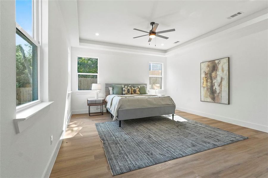 Bedroom with a tray ceiling, light wood finished floors, ceiling fan, and recessed lighting