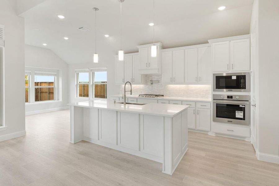 White kitchen with large center island, stainless steel appliances, pendant lights, and light wood floors
