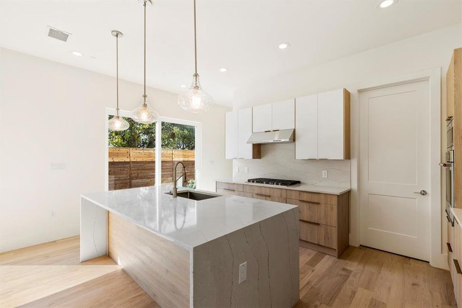 Kitchen featuring light hardwood / wood-style flooring, a center island with sink, sink, gas stovetop, and white cabinets