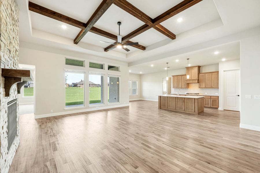 Open-concept living area with coffered beam ceiling, stone fireplace, and kitchen with island and wood cabinets Open-concept living area with coffered beam ceiling, stone fireplace, and kitchen with island and wood cabinets