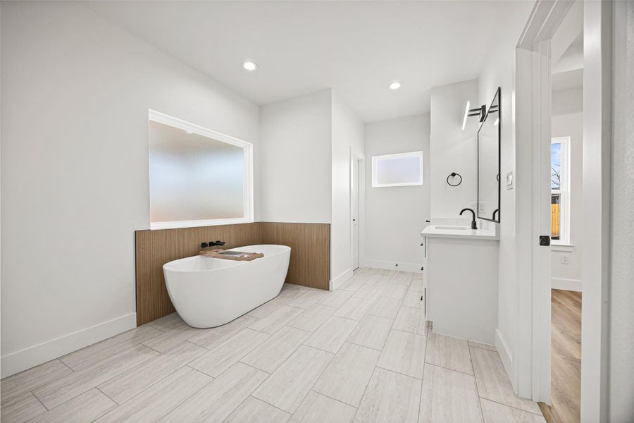 Freestanding soaking tub with fluted tile accent wall in a warm wood-look finish and private frosted window for natural light and privacy.
