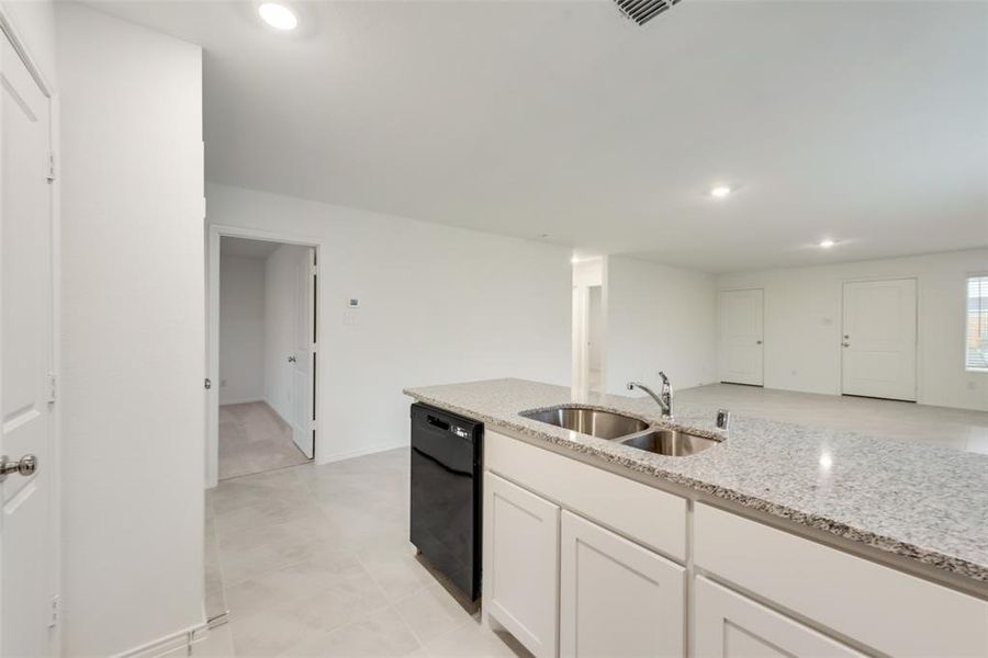 Kitchen featuring light tile patterned flooring, white cabinets, sink, black dishwasher, and light stone counters