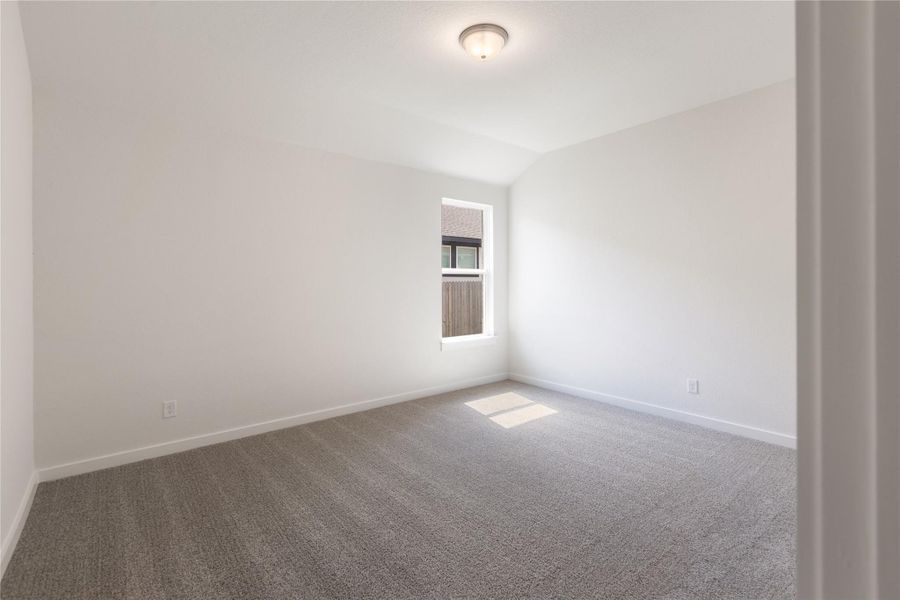 Carpeted empty room featuring lofted ceiling and baseboards