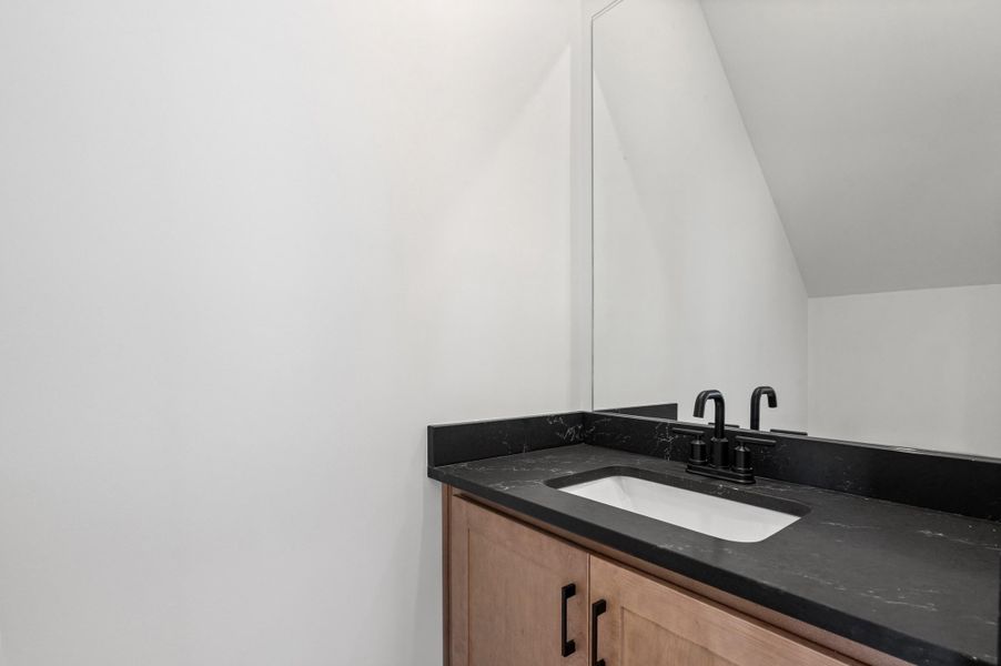Vanity with wood-finish cabinetry, dark countertop, integrated rectangular sink, and matte black faucet