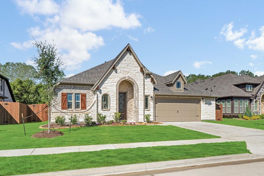 Single-story home with cream stone and brick exterior, arched entry, two-car garage, and green front lawn.