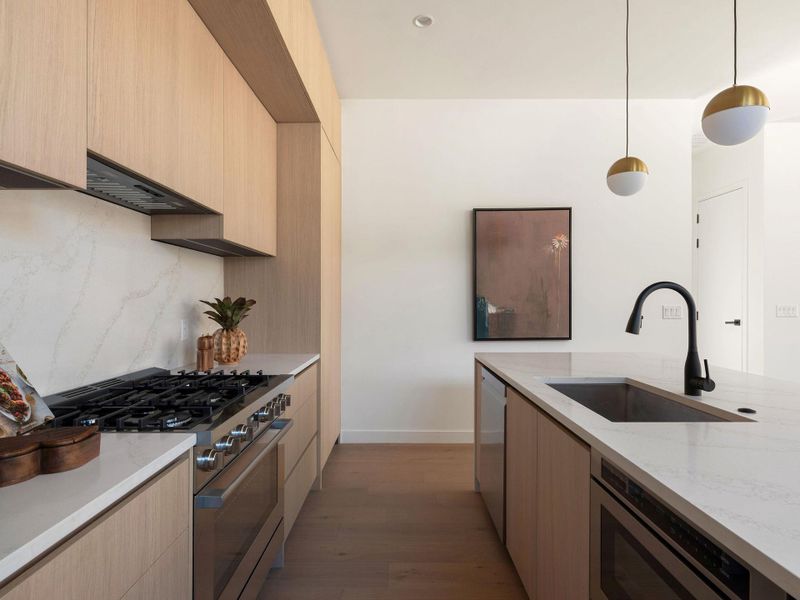 Kitchen featuring light stone countertops, stainless steel appliances, modern cabinets, pendant lighting, and light wood finish cabinets